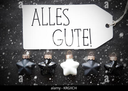 Etikett mit deutschem Text alles Gute, die besten Wünsche. Schwarze und Weiße Christbaum Kugeln auf schwarzem Papier Hintergrund mit Schneeflocken. Weihnachtsdekoration oder Textur. Flach anzeigen Stockfoto