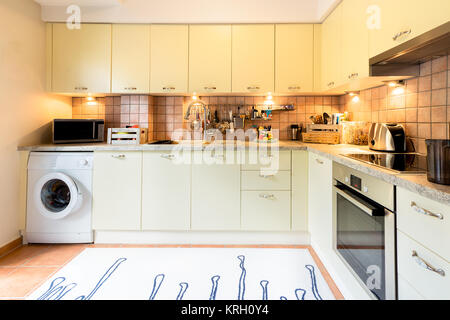 Eine moderne Küche mit Laminat Einbauschränke und Schränke, Waschmaschine, Herd, Mikrowelle und Kochutensilien. Stockfoto