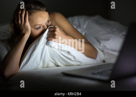 Hübsche junge Frau, die gerade etwas schrecklich/sad auf ihrem Laptop im Bett Stockfoto