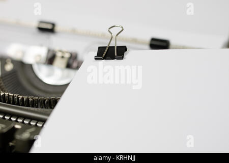 Eine weiße Karte mit einer Büroklammer auf einer Schreibmaschine. Papier mit einem Clip auf einer alten Schreibmaschine. Weißer Hintergrund. Stockfoto