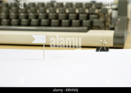 Eine Fahne von Papier in ein weißes Blatt Papier geklebt. Eine weiße Karte und eine Schreibmaschine im Hintergrund. Weißer Hintergrund. Stockfoto