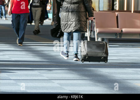 Frau in schwarzem Mantel und Koffer geht mitten unter anderen Menschen rund um den Flughafen Wartebereich an Bord des Flugzeugs. Stockfoto