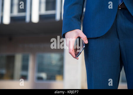 Gesichtslosen Schuß von Mann im schicken Anzug holding Telefon beim Stehen mit Hand in der Tasche auf der Straße. Stockfoto