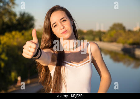 Glücklich aussehende junge Frau im Park an einem sonnigen Tag und deutete mit dem Daumen nach oben. Stockfoto