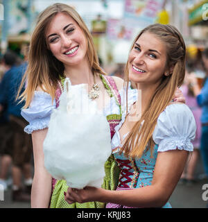 Zwei junge Frauen im Dirndl Kleid oder Tracht, lächelnd mit Baumwolle Zuckerwatte auf dem Oktoberfest Stockfoto