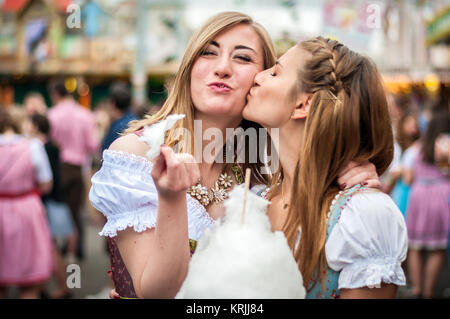 Zwei junge Frauen in Dirndl oder Tracht, Küssen mit Baumwolle Zuckerwatte auf dem Oktoberfest Stockfoto