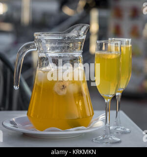 Gelbe Champagner Sangria serviert in einem Becher mit zwei Gläsern Stockfoto