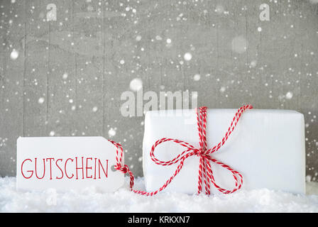 Ein Weihnachtsgeschenk auf Schnee. Zement Wand als Hintergrund mit Schneeflocken. Moderne und den urbanen Stil. Karte für den Geburtstag oder Seasons Greetings. Etikett mit deutschem Text Gutschein bedeutet Gutschein Stockfoto