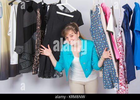 Fröhliches junges Mädchen blickte von der Kleidung auf Bügeln hängend Stockfoto