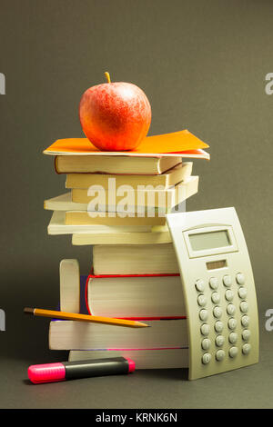 Begriff der Bildung. Stapel Schulbücher mit Rechner, rosa Markierung und Bleistift und einen roten Apfel auf der Oberseite Vor dunkelgrauem Hintergrund Stockfoto
