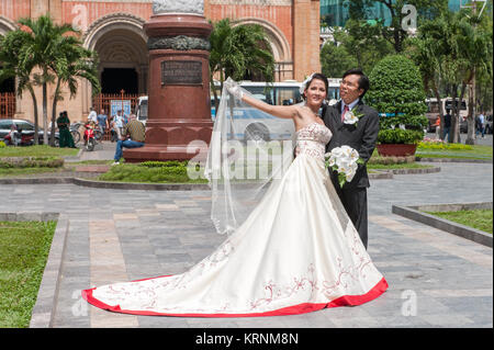 Hochzeit paar außerhalb der Kathedrale Notre Dame in Saigon posieren. Die vietnamesischen Bräute normalerweise in drei verschiedene Kleider während der Rezeption. Stockfoto