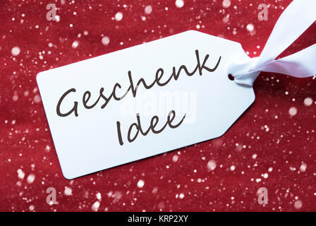 Deutsche Text Geschenk Idee bedeutet Geschenk Idee. Eine White Label auf einem Roten strukturierten Hintergrund. Tag mit Band und Schneeflocken. Stockfoto