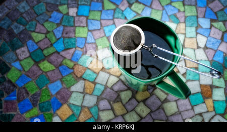 Eine Tasse Kaffee mit einem Teesieb auf einem Mosaik Tisch Stockfoto