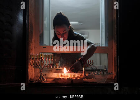 Eine religiöse jüdische Frau leuchtet ein Olivenöl Kerze auf einem menorah Kandelaber auf der Fensterbank Ihres Hauses während der jüdische Feiertag von Chanukka, das Lichterfest, am jüdischen Viertel in der Altstadt Jerusalem, Israel Stockfoto