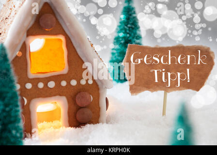 Deutsche Text Geschenk Tipp bedeutet Geschenk Tipp. Lebkuchenhaus in der verschneiten Landschaft als Weihnachtsdekoration. Bäume und Kerzenlicht für eine romantische Atmosphäre. Silberner Hintergrund mit Bokeh Wirkung. Stockfoto