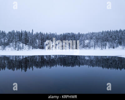 Schöne verschneite Winterlandschaft von einem Wald über eine Ungefroren Wasser im Oulanka National Park. Ruka, Finnland. Stockfoto