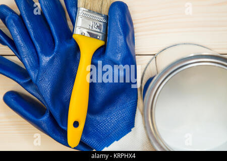 Schutz für die Renovierung. Ein paar blaue Latex Handschuhe, eine Bürste und eine Blechdose weißer Ölfarbe auf ein leichtes weißes Holz- Hintergrund. Schließen Stockfoto