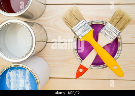 Bereit, ein Haus zu malen. Eine Blechdose von fuchsia Ölfarbe mit gekreuzten Bürsten auf der Oberseite, Baum Farbdosen auf der linken Seite, leicht ungefärbt Holz- Hintergrund. Stockfoto