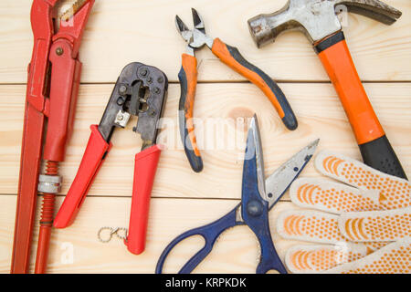 Renovieren ein Haus. Eine Reihe von hellen Reparatur Werkzeuge - pilers, Schere, ein Hammer und ein Paar Schutzhandschuhe auf einem farblosen Holz- Hintergrund, c Stockfoto