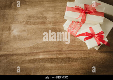 Vintage Kraftpapier Kartons mit Geschenken, mit roten Bändern auf rustikalen Holzmöbeln Hintergrund gebunden. Stockfoto