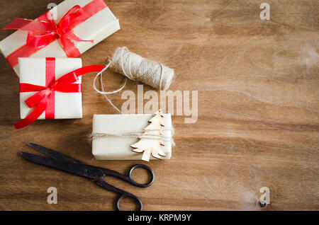 Vintage Kraftpapier Kartons mit Geschenken, mit roten Bändern und Jute mit Holz Weihnachtsbaum auf rustikalen Hintergrund gebunden. Stockfoto