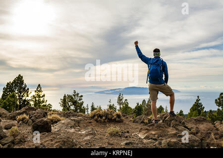 Mann feiern Sonnenuntergang an der Blick in die Berge. Trail Runner, Wanderer oder Bergsteiger erreicht oben auf einem Berg, geniessen Sie inspirierende Landschaft auf felsigen Stockfoto