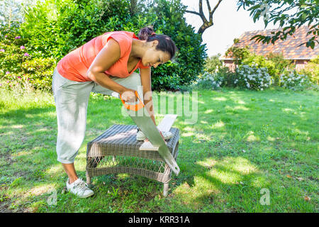 Junge kolumbianische Frau Sägen von Holz mit handsäge Outdoor Stockfoto