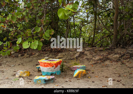 Ein Schleiftisch mit Einrückung und Stein Grinder aus bunt bemalten Stücke aus Beton und Steine am Strand und tropischen Pflanzen in der Stockfoto