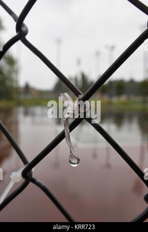 Einen kleinen Kabelbinder an einem Maschendrahtzaun mit einem Tropfen Wasser Stockfoto