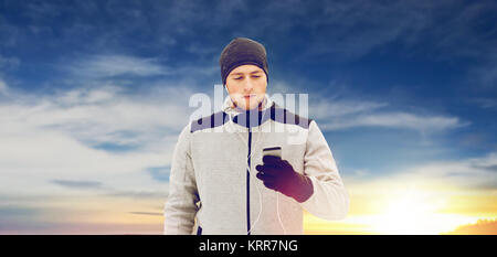 glücklicher Mann mit Kopfhörern und Smartphone im winter Stockfoto