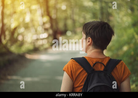 Ansicht der Rückseite des Erwachsenen kaukasischen Frauen mit Rucksack beim Spaziergang im Park auf sonnigen Sommernachmittag. Gesunder Lebensstil, Erholung und Natur lovi Stockfoto