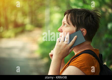 Frau Gespräch am Handy im Park, erwachsene Frau backpacker Walking im Freien und Sie ihr Smartphone für die Kommunikation. Stockfoto