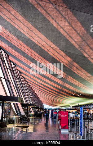 DULLES International Airport Terminal Interior Chantilly Virginia // DULLES, Virginia — das Sonnenlicht am späten Nachmittag strömt durch große Glasfenster auf die Decke des ursprünglichen flügelförmigen Terminalgebäudes am Dulles International Airport in Chantilly, Virginia. Das vom renommierten Architekten Eero Saarinen entworfene und 1962 eröffnete Hauptterminal ist bekannt für sein unverwechselbares, geschwungenes Dachdesign. Dulles ist einer von drei großen Flughäfen in der Metropolregion Washington DC, die sowohl nationale als auch internationale Flüge abwickelt. Das modernistische Gebäude gilt als architektonisches Landhaus Stockfoto
