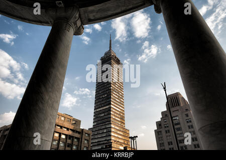 Torre Latinoamericana von den Säulen des Palacio de Bellas Artes eingerahmt, Mexiko-Stadt | MEXIKO-STADT, Mexiko — Zwischen zwei Marmorsäulen des Palacio de Bellas Artes eingerahmt, steht in der Ferne die Torre Latinoamericana, eine Kombination aus dem 1934 im Art-Nouveau-Art-Deco-Stil erbauten Palast und dem 1956 im internationalen Stil von Augusto H. Álvarez entworfenen Turm. Der Palast, vom italienischen Architekten Adamo Boari erbaut und von Federico Mariscal vollendet, ist etwa 13 Fuß (4 m) unter dem Straßenniveau abgesunken, ein Beweis für die unterschiedliche Senkung, die das historische Zentrum von Mexiko-Stadt prägt. Stockfoto