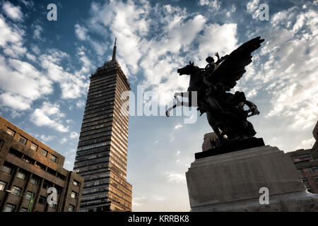 Pegasus Statue Torre Latinoamericana Mexico City // MEXIKO-STADT, Mexiko — eine der vier Pegasus-Statuen des spanischen Bildhauers Agustín Querol steht auf der Plaza de Bellas Artes mit dem Torre Latinoamericana im Hintergrund. Diese dynamischen geflügelten Pferdeskulpturen mit Reitern wurden ursprünglich für die Dachlinie des Palacio de Bellas Artes während der frühen Entwurfsphase unter dem Architekten Adamo Boari in Auftrag gegeben. Die Bronzestatuen wurden in Madrid gegossen und kamen zwischen 1910 und 1911 während der letzten Jahre des Porfirio Díaz-Regimes in Mexiko an. Nach der Fertigstellung des Gebäudes bildet der Pegasus-Sculp Stockfoto