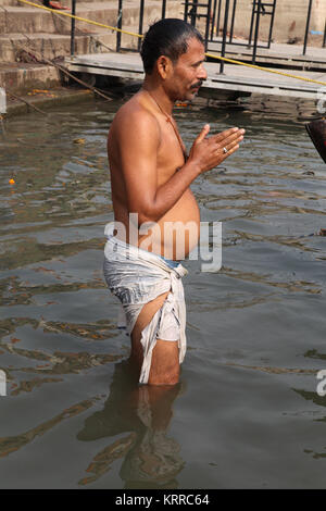 Ein männlicher Pilger mit einem Topf Bauch betet in den Ganges in Varanasi, Indien Stockfoto