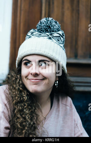 Lächelnd junges Mädchen mit langen, lockigen Haar zu tragen Stricken hat Stockfoto