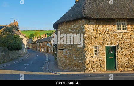 Streetscene im schönen Dorset Dorf Abbotsbury, mit strohgedeckten Hütten unter einem blauen Himmel. Stockfoto