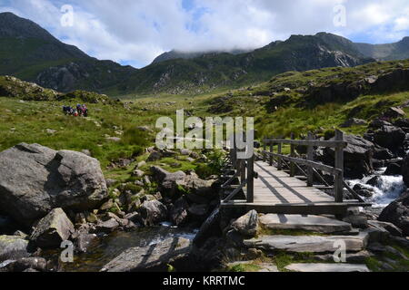 Gruppe der Wanderer nähert sich die Brücke über Stream am Llyn Ogwen vom Mount Tryfan, Snowdonia, Wales, Großbritannien Stockfoto