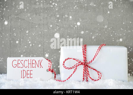 Etikett mit deutschem Text Geschenk Idee bedeutet Geschenk Idee. Ein Weihnachtsgeschenk auf Schnee. Zement Wand als Hintergrund mit Schneeflocken. Moderne und den urbanen Stil. Stockfoto