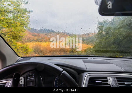Regen fällt auf die Fenster des Autos. herbstlich verregnete Landschaft verschwommen Stockfoto