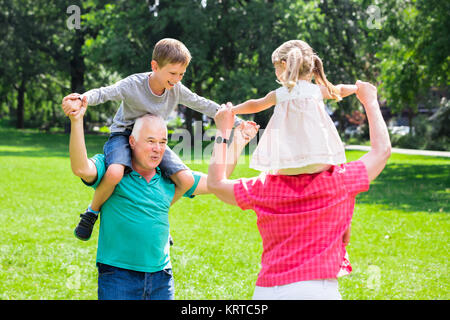 Großeltern und Enkel Piggyback Ride in Park Stockfoto