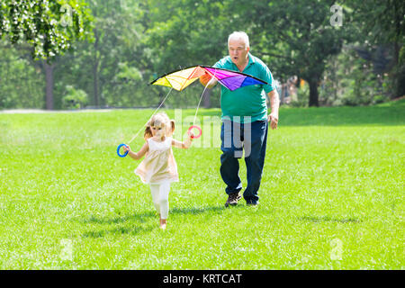 Enkelin und Großvater fliegende Drachen in Park Stockfoto
