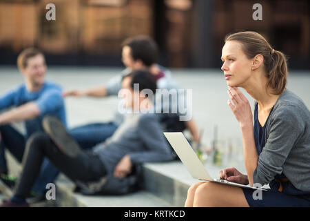 Porträt einer schlanken jungen Frau mit Laptop Computer, nachdenklich im Stadt/Ort Kontext (flacher DOF Farbe getonte Bild) Stockfoto