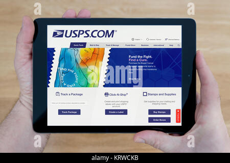Ein Mann schaut auf der United States Postal Service Website (USPS.com) auf einem iPad Tablet, Schuß gegen einen hölzernen Tisch top Hintergrund (nur redaktionelle Nutzung) Stockfoto