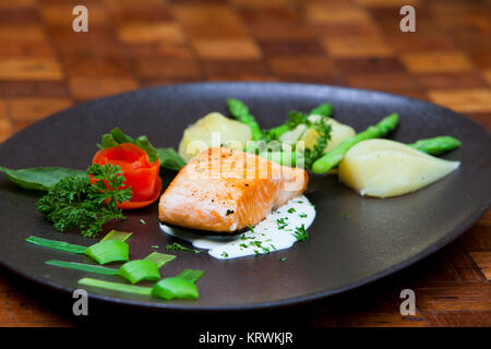 Atlantischer Lachs mit Rucola, mit Gemüse auf einer schwarzen Platte eingerichtet. Stockfoto