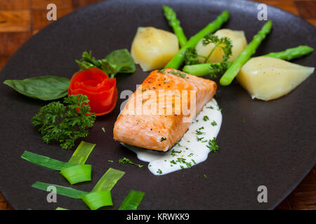 Atlantischer Lachs mit Rucola, mit Gemüse auf einer schwarzen Platte eingerichtet. Stockfoto