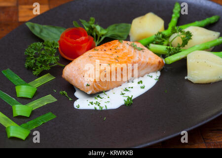 Atlantischer Lachs mit Rucola, mit Gemüse auf einer schwarzen Platte eingerichtet. Stockfoto