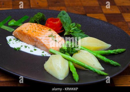 Atlantischer Lachs mit Rucola, mit Gemüse auf einer schwarzen Platte eingerichtet. Stockfoto