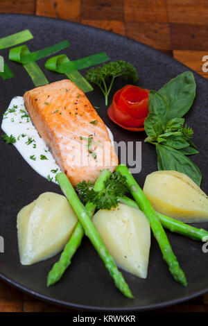 Atlantischer Lachs mit Rucola, mit Gemüse auf einer schwarzen Platte eingerichtet. Stockfoto